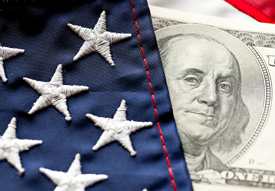 A closeup of part of an American flag next to a $100 dollar bill showing Benjamin Franklin's face.