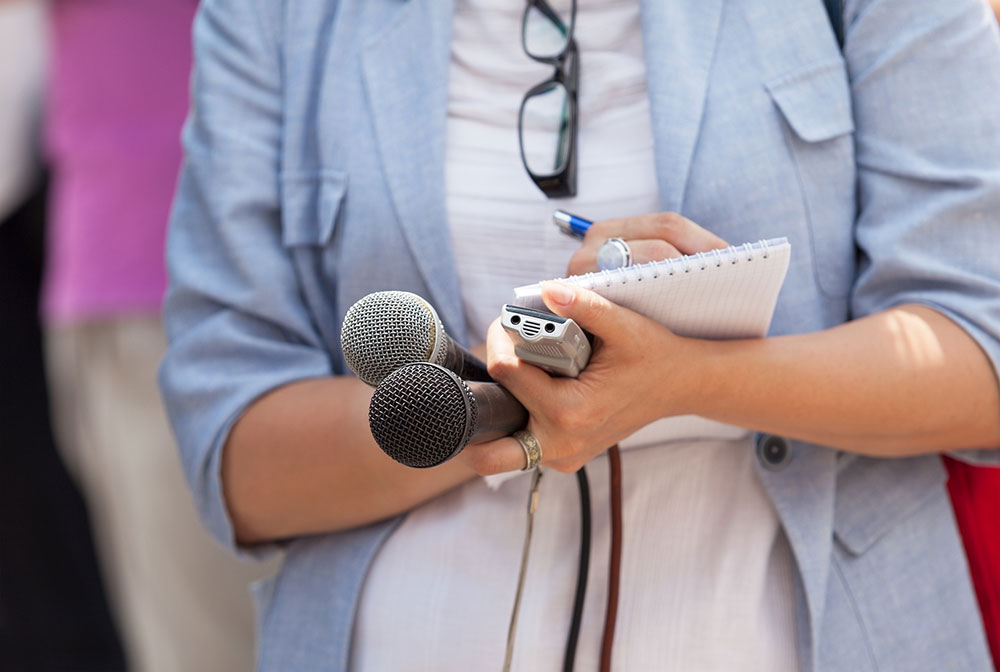 Close-up of reporter's hands holding microphone, recorder and steno pad.